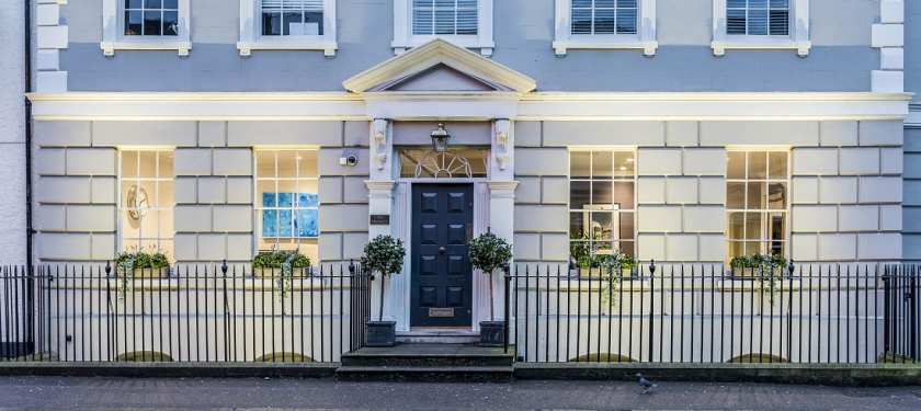 The Townhouse on Fore Street, Hertford, a Georgian frontage with a dark front door, lit windows and bay trees either side of the steps.